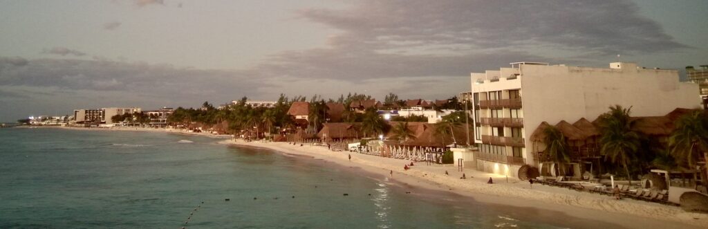 Drone view of Playa del Carmen's coastline and beach clubs at sunrise, showcasing golden hues, tranquil turquoise waters, and the vibrant beachfront of the Riviera Maya