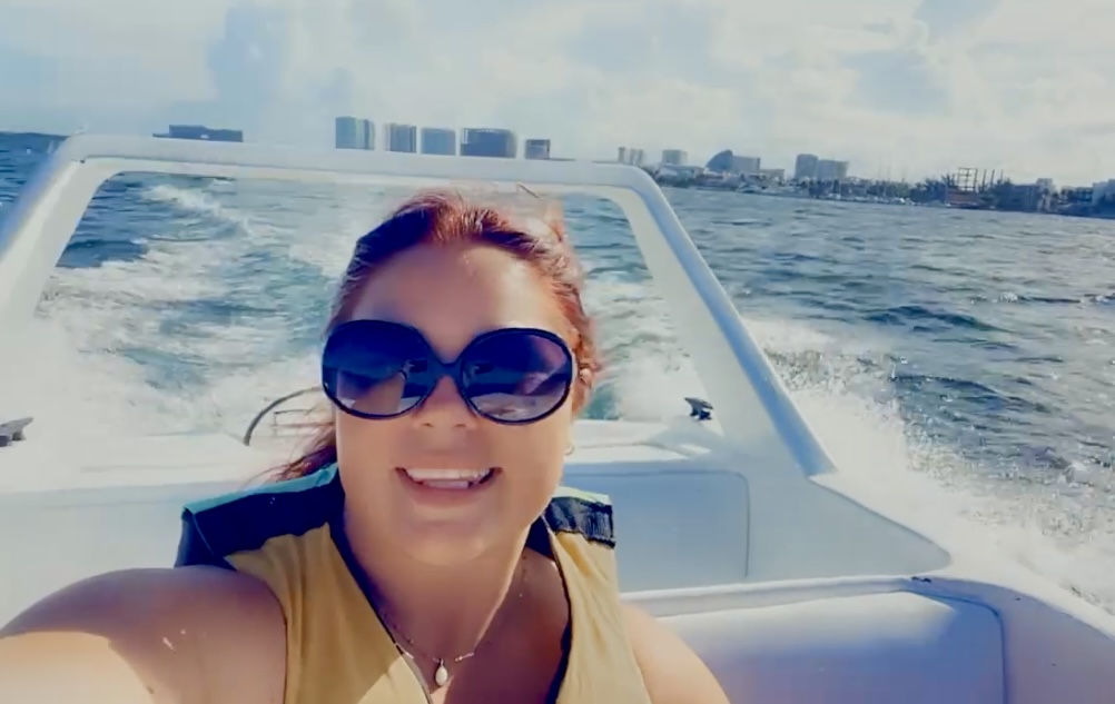 Travel blogger Mackenzie on a speedboat tour in Cancun, Mexico, with a stunning view of Cancun's skyline and turquoise waters in the background, showcasing adventure and Caribbean travel