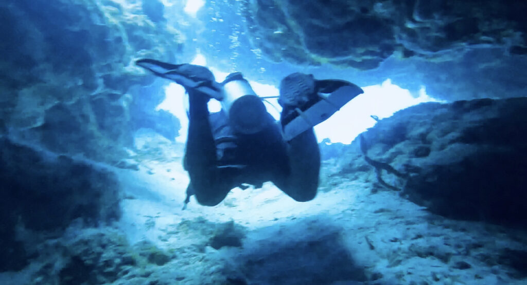 Scuba diver exploring an underwater swim-through site off the coast of Cozumel, Mexico, surrounded by vibrant coral reefs and clear turquoise waters, highlighting adventure and marine life in the Caribbean.