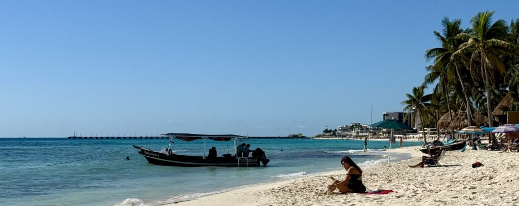 Beautiful beach at 38th Street in Playa del Carmen, Mexico, featuring turquoise waters, soft sand, and the ferry pier visible in the background, capturing the charm of the Riviera Maya coastline