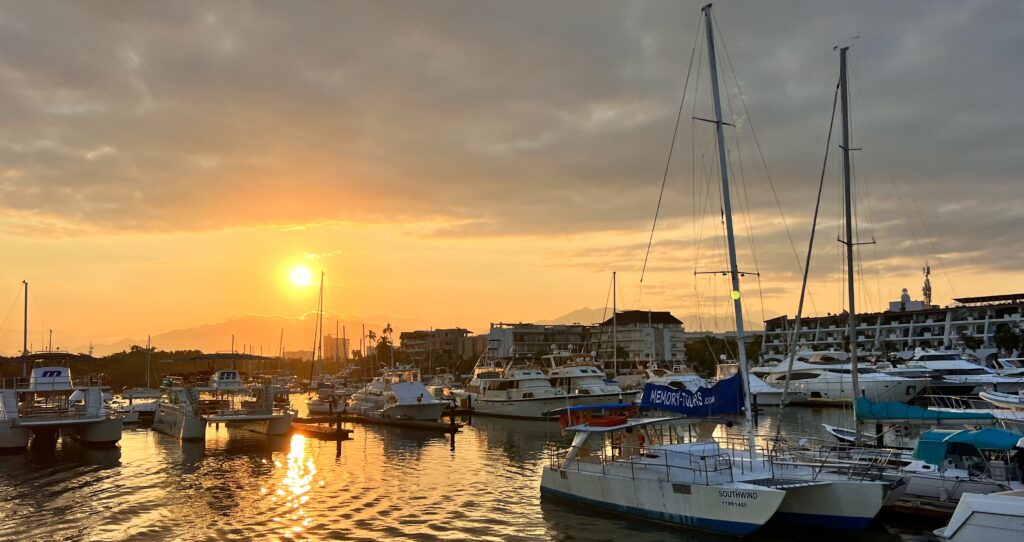 Sunset over a boat harbor in Puerto Vallarta, showcasing mountains in the background and the reflection of the boats in the calm waters