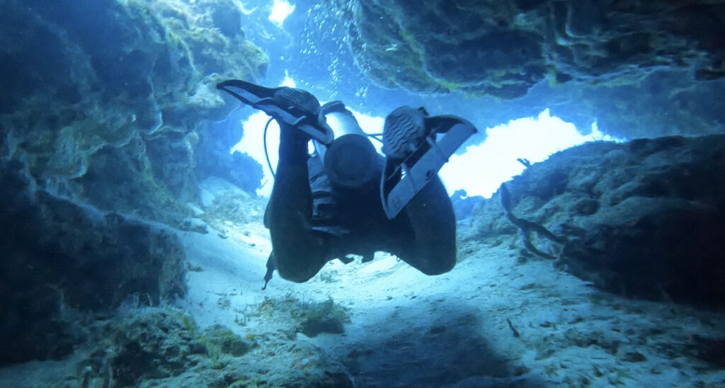 Scuba instructor guiding through a stunning swim-through site with crystal-clear, vibrant blue waters in Cozumel, offering an unforgettable underwater adventure