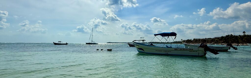 Clear turquoise waters in Akumal with boats gently floating in the background, creating a tranquil coastal scene