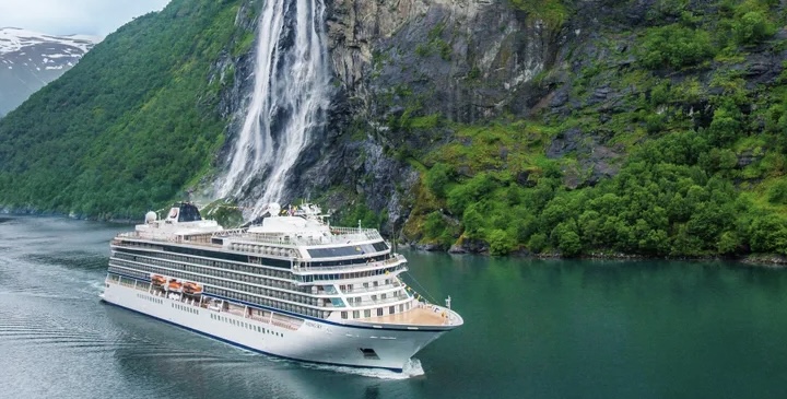 A Viking cruise ship gliding peacefully down a serene river with a majestic waterfall cascading into the distance, surrounded by lush greenery and tranquil waters, creating a picturesque and serene environment.