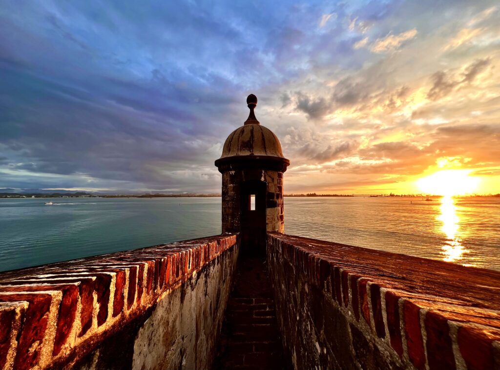 Castillo San Felipe del Morro in Old San Juan, Puerto Rico, with a stunning sunset on one side and storm clouds rolling in from the other, creating a dramatic coastal scene.