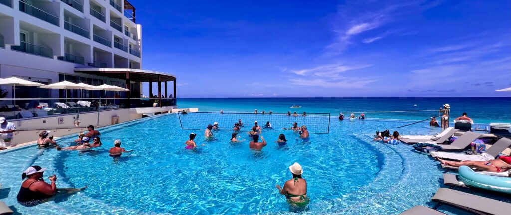 Infinity pool meeting the Caribbean Sea at Sun Palace Resort, right next to the pool bar and restaurant, with people playing volleyball in the activity pool