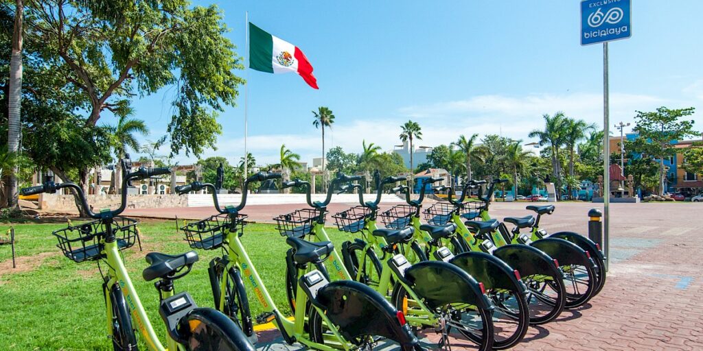 Biciplaya app bikes ready to be used, featuring a Mexican flag in the background, highlighting the bike rental service in Playa del Carmen.