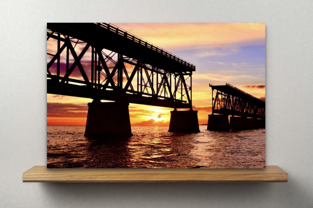 Bahia Honda Bridge at sunset, featuring vibrant hues of blue, yellow, and orange as the sun sets behind the bridge, creating a stunning, picturesque view with a break in the middle