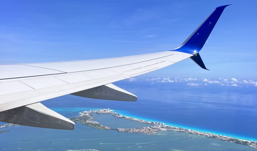 Airplane wing soaring above Cancun’s Hotel Zone (The 7), offering a breathtaking view of the turquoise coastline and crystal-clear Caribbean Sea