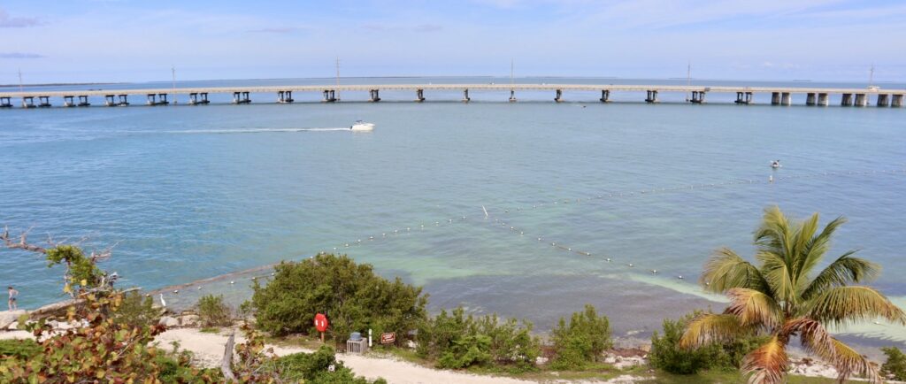 View from the top of Bahia Honda Bridge, looking out over the water towards the long bridge leading to Key West, with expansive views of the Florida Keys