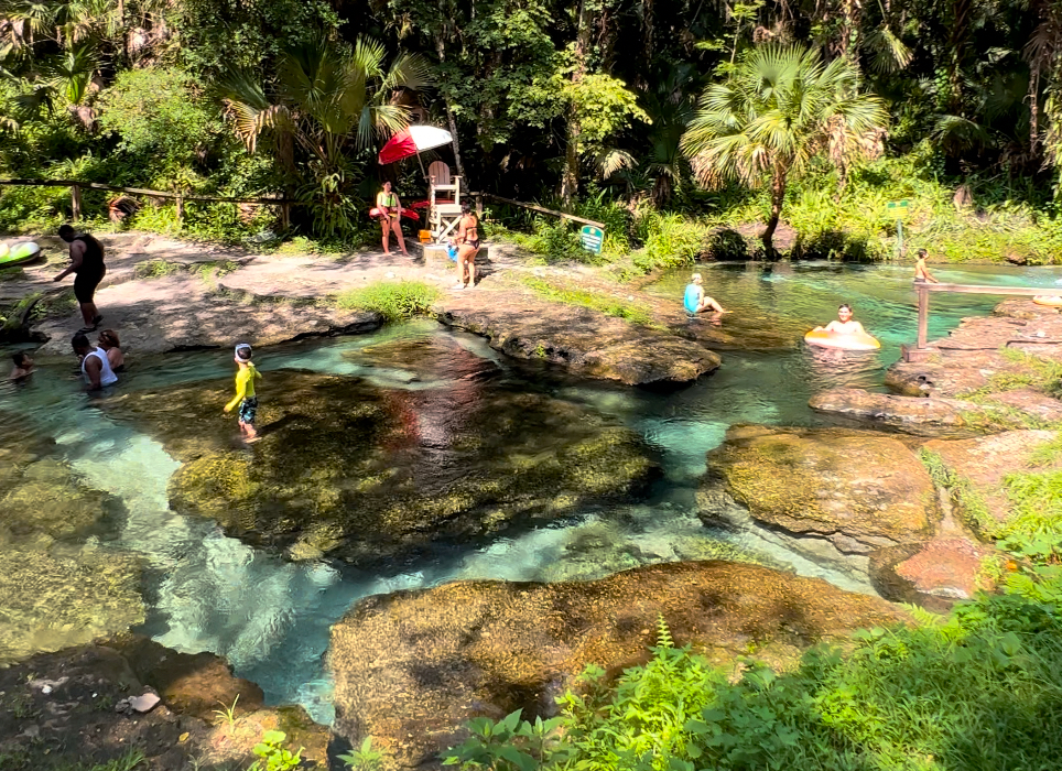 Top area of Kelly Park Rock Springs in Florida, with people relaxing in tubes, enjoying the clear spring water, and a lifeguard standing in the background
