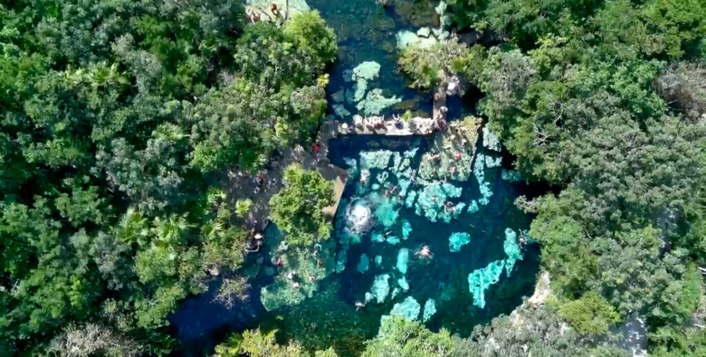 Aerial view of Cenote Azul captured by drone, showcasing the vibrant blue-green waters surrounded by lush trees and natural greenery