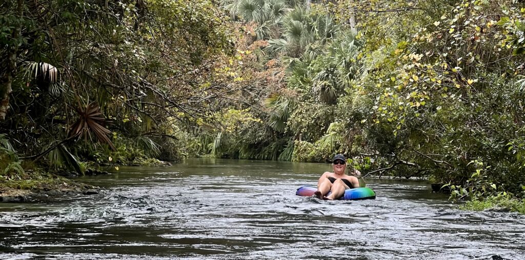 Mom floating down the spring river at Kelly Park Rock Springs in Florida, smiling with tropical greenery surrounding the clear waters