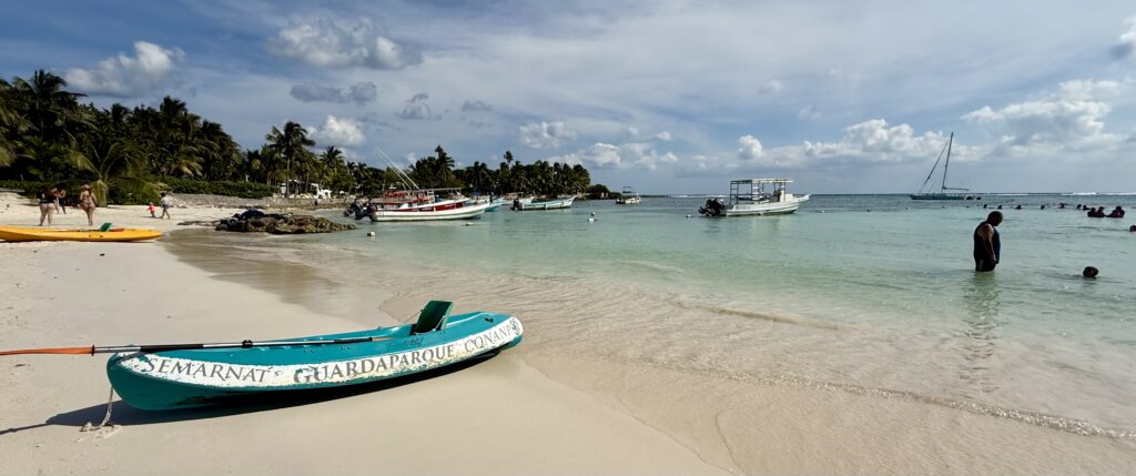 Beach in Akumal, Mexico, featuring clear turquoise waters, boats in the background, and a kayak in the foreground, ready for adventure