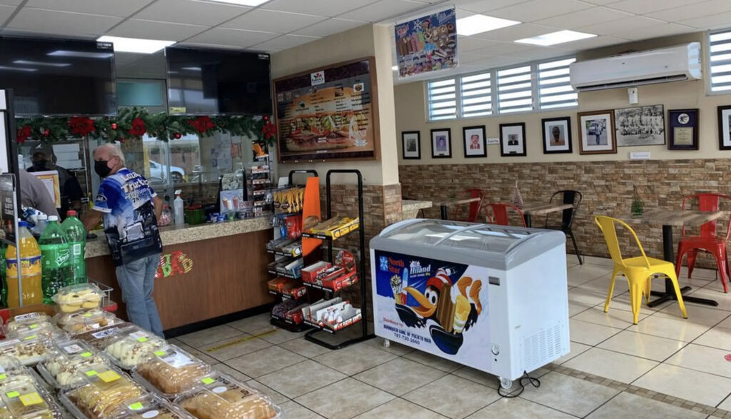 Inside Palmas Bakery in Puerto Rico, featuring a sitting area with tables, an ice cream case, pastries on display, and the order counter