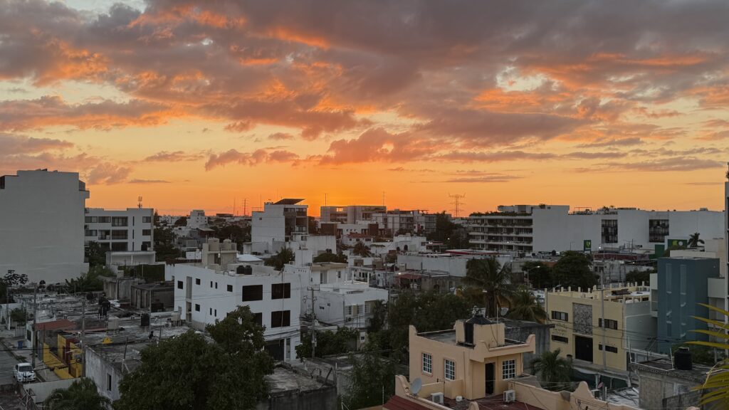 Rooftop view of Playa del Carmen at sunset, with orange skies casting a warm glow over the city streets and buildings, stretching five blocks into the vibrant Riviera Maya landscape