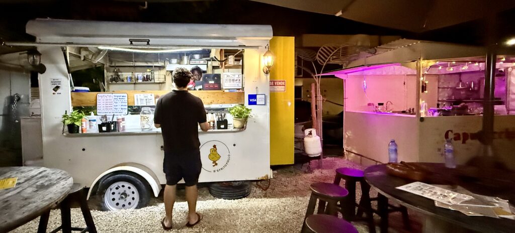 The BS Frito Pollo food truck serving fried chicken, with a customer standing nearby waiting for their order, capturing the essence of local flavors in Playa del Carmen.