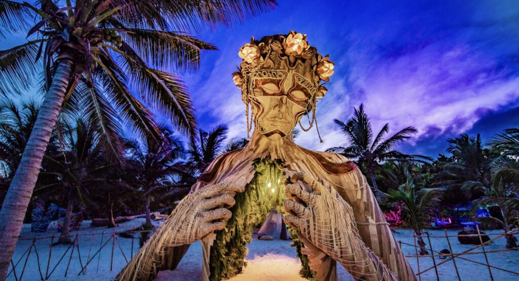 The iconic Ah Cacao Maya Ruins wooden sculpture in Tulum, featuring an open chest design, set against a backdrop of tropical greenery