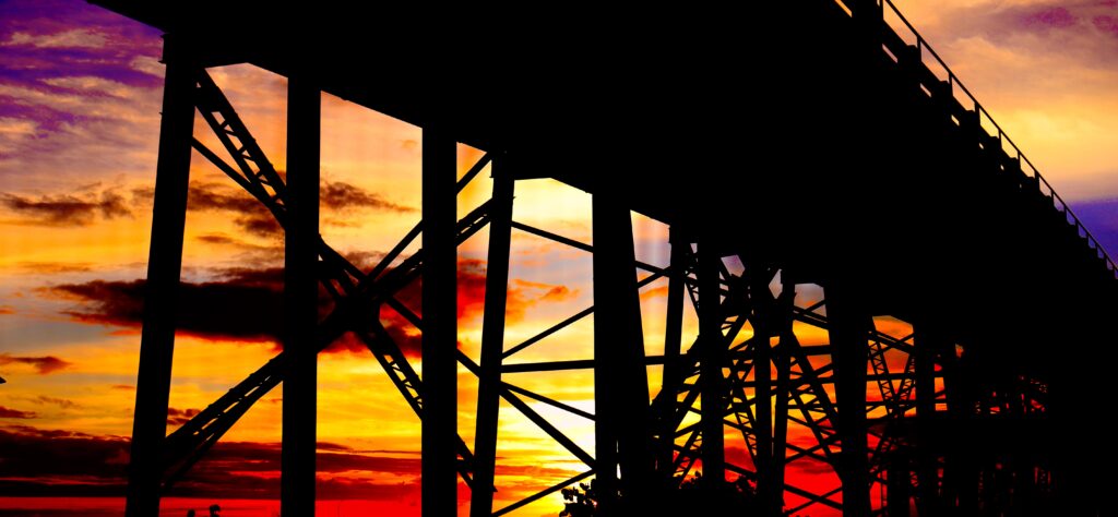 Sunset setting behind Bahia Honda Bridge with vibrant colors, including purples, blues, oranges, reds, and yellows, creating a stunning and colorful backdrop