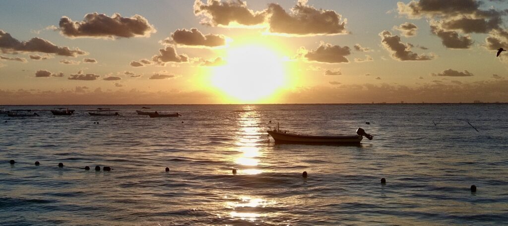 Drone view of a breathtaking Caribbean sunrise with vibrant orange and pink hues over the turquoise waters, featuring a small speedboat gliding across the tranquil sea near Playa del Carmen